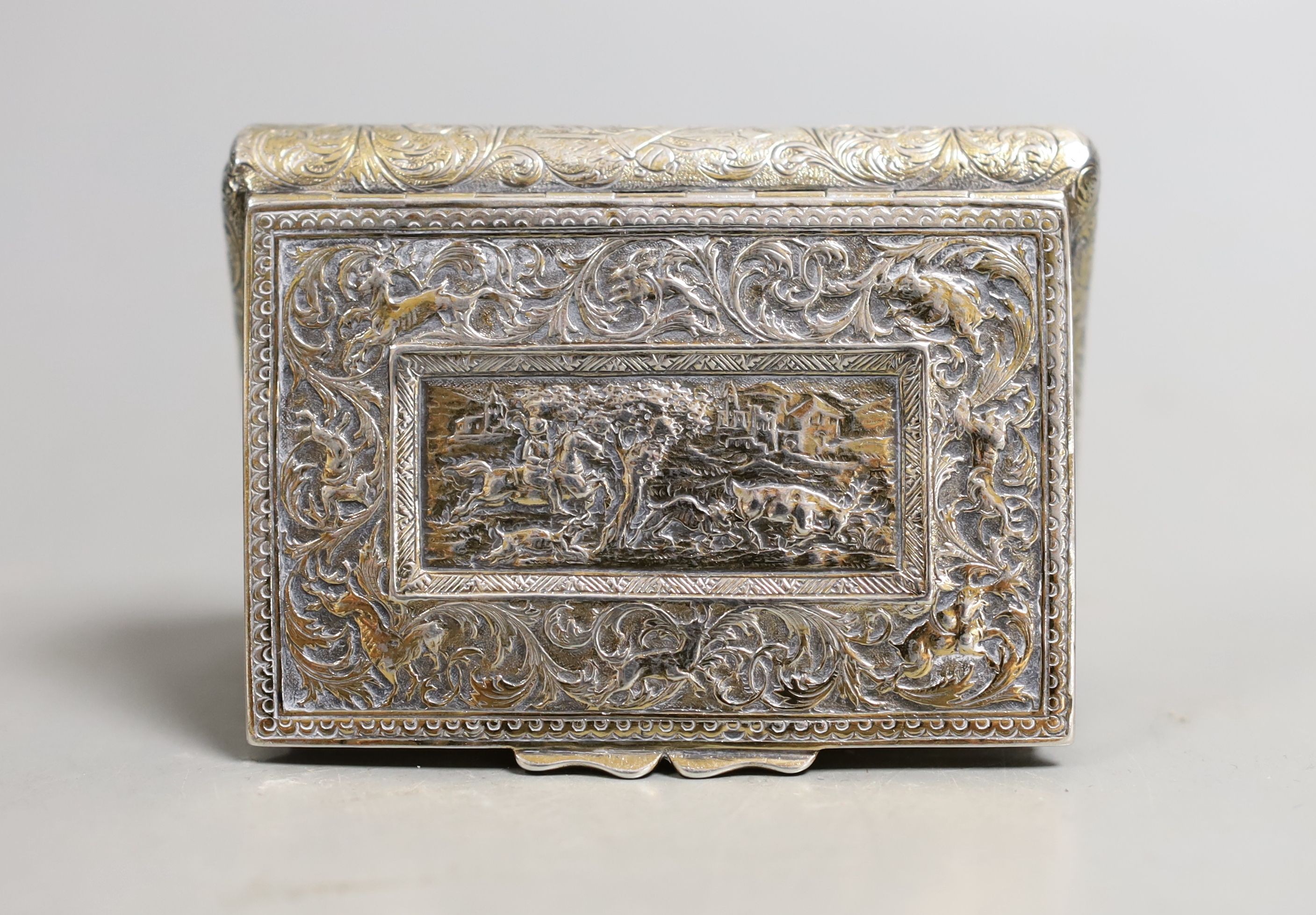 A 19th century continental gilt white metal rectangular bombe shaped snuff box, embossed with foliate scrolls and central stag hunting scene, unmarked, 81mm.